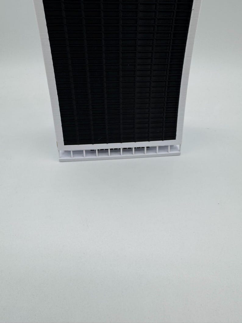 May include: A white and black air filter with a grid pattern. The filter has a white plastic frame and a black mesh insert.