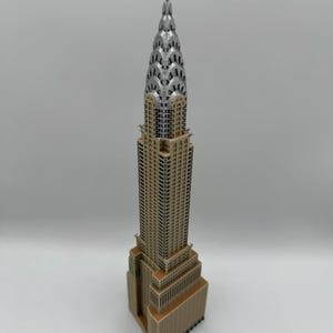 May include: A detailed model of the Chrysler Building, a famous Art Deco skyscraper. The model features a silver spire and a tan and brown facade, showcasing the building's distinctive architectural details. The model is a miniature replica of the iconic New York City landmark.