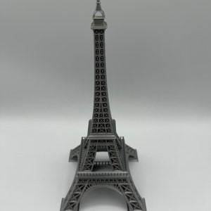 May include: A gray metal Eiffel Tower model. The model is detailed with intricate latticework and a pointed spire.