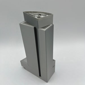 May include: A gray 3D printed model of a tall building with a flat roof. The building has a rectangular shape with a slightly curved top.