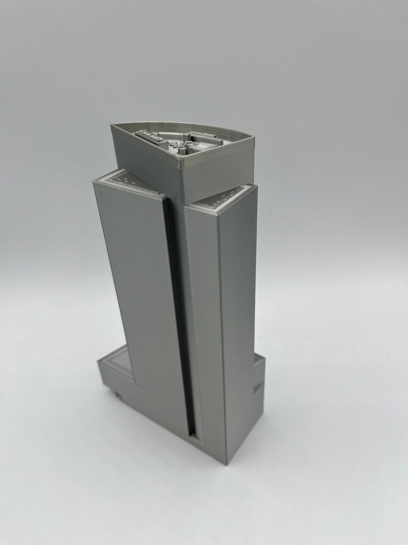 May include: A gray 3D printed model of a tall building with a flat roof. The building has a rectangular shape with a slightly curved top.