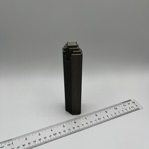 May include: A dark gray metal sculpture of a building with a stacked design. The sculpture is about 6 inches tall and is sitting on a white surface.
