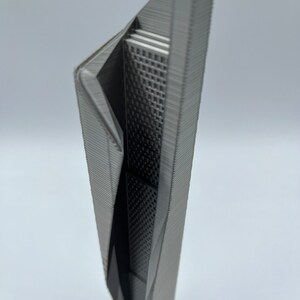 May include: A 3D printed model of a modern skyscraper with a unique, angular design. The model is made of a gray plastic and has a detailed exterior.