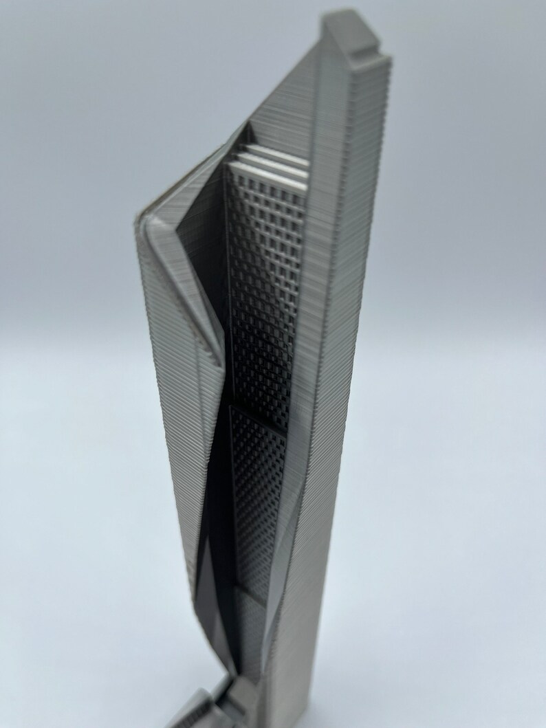 May include: A 3D printed model of a modern skyscraper with a unique, angular design. The model is made of a gray plastic and has a detailed exterior.