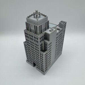 May include: A gray, miniature model of a skyscraper with the text "EASTERN" on the top. The building has a detailed facade with many windows and architectural features. The model is a detailed representation of a classic building.