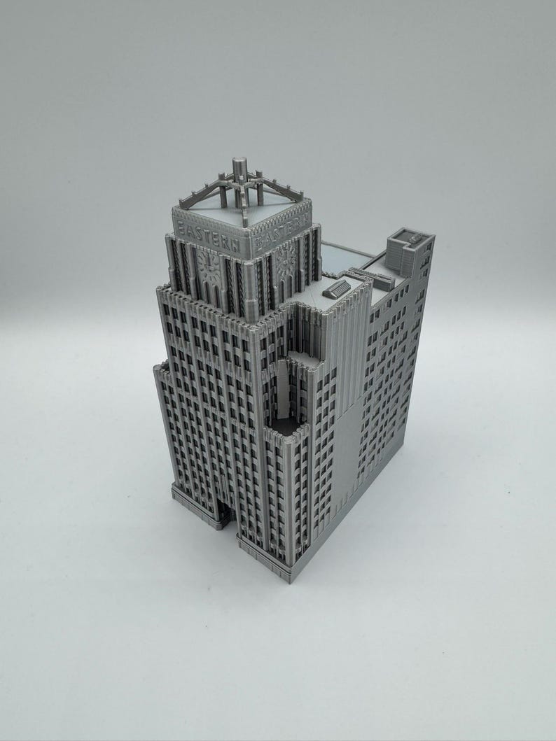 May include: A gray, miniature model of a skyscraper with the text "EASTERN" on the top. The building has a detailed facade with many windows and architectural features. The model is a detailed representation of a classic building.
