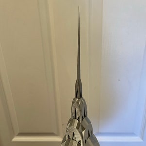 May include: A silver 3D printed model of the Chrysler Building in New York City. The model is detailed and features the building's iconic spire.