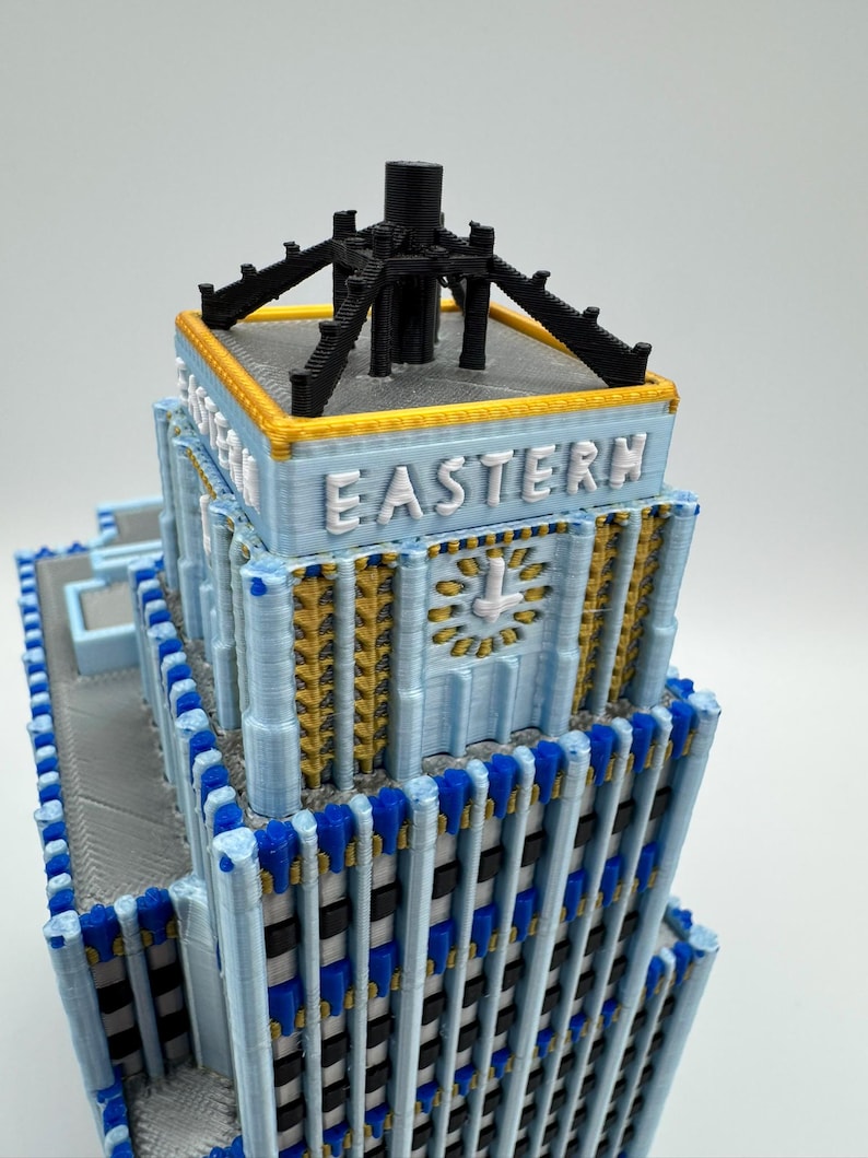 May include: A 3D-printed model of a building with the word "EASTERN" in white letters. The building features a light blue facade with gold and blue accents. The top has a black structure.