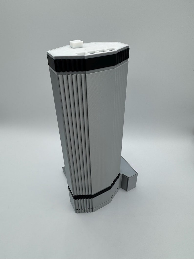 May include: A silver-colored, geometric knife block with a white top and black accents. The knife block has a rectangular base and a tall, multi-sided body with vertical grooves. A small, white square is on top.