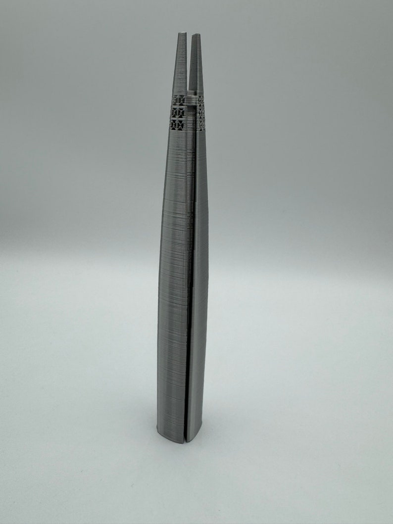 May include: A 3D printed model of a skyscraper, made of gray plastic. The model is detailed with windows and a textured surface.