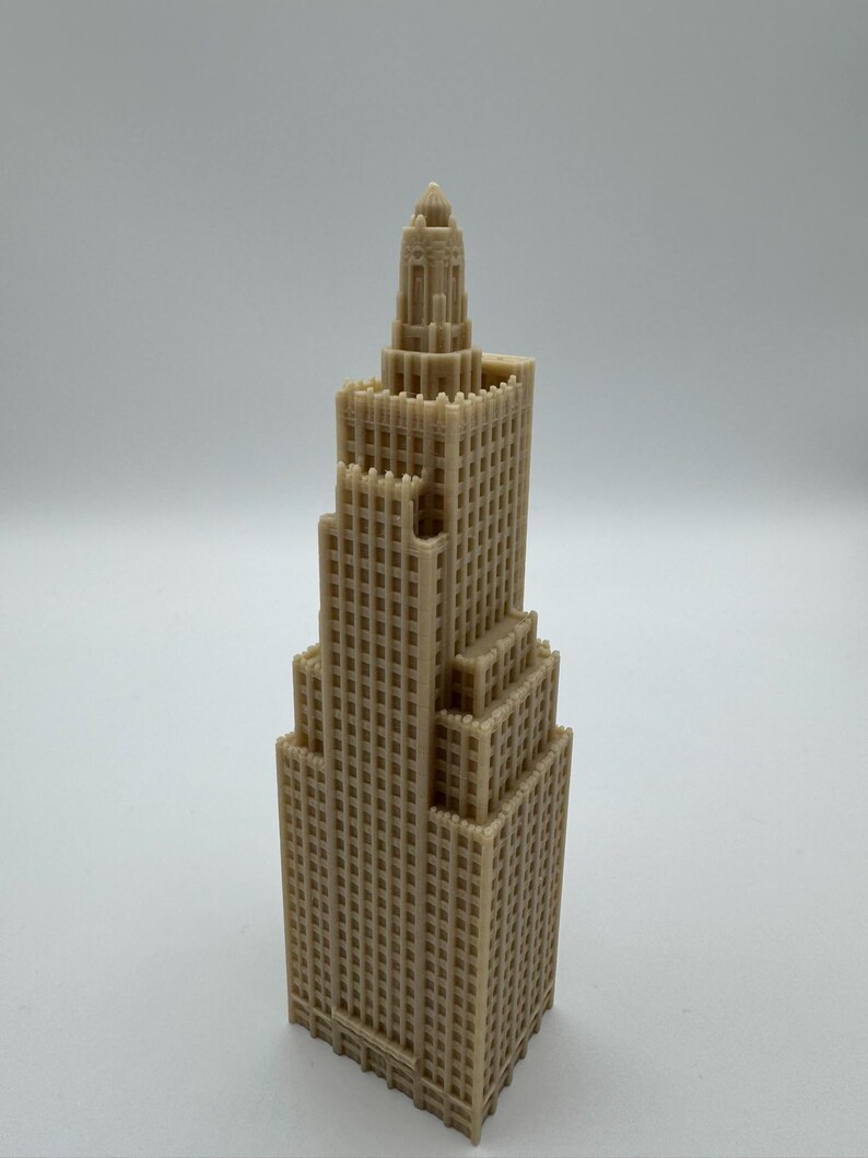 May include: A tan-colored miniature skyscraper model with a detailed, multi-tiered design. The building features numerous windows and architectural details, showcasing a classic skyscraper aesthetic. The model is a solid, three-dimensional object.