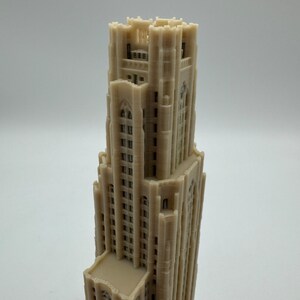 May include: A 3D printed model of a tall, beige building with a pointed roof and many windows. The building has a detailed facade with intricate carvings and decorative elements.