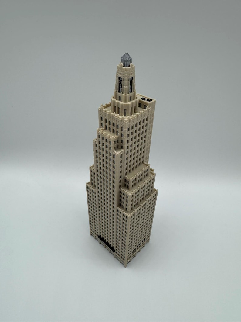May include: A beige, miniature skyscraper model with a detailed design. The building has multiple tiers and a decorative top. The model is made of a light-colored material and features numerous small windows. The overall design is reminiscent of classic architecture.