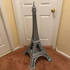 May include: A gray Eiffel Tower model, a detailed replica of the iconic Parisian landmark. The tower features intricate lattice work and a pointed spire, standing tall against a neutral background. This decorative piece is a symbol of Paris.