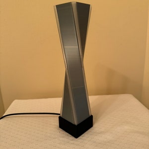 May include: A black and gray geometric lamp with a twisted design. The lamp has a black base and a clear cord.