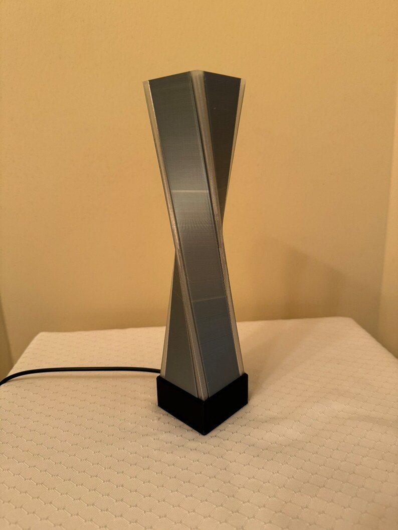 May include: A black and gray geometric lamp with a twisted design. The lamp has a black base and a clear cord.