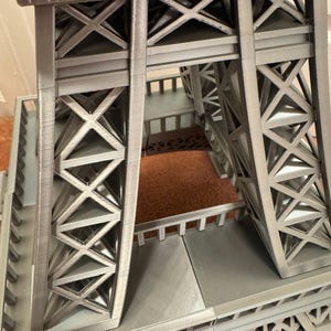 May include: A detailed, gray model of the Eiffel Tower, showcasing its intricate lattice structure. The image highlights the tower's architectural design, with visible cross-bracing and support beams. The model is a miniature representation of the iconic landmark.