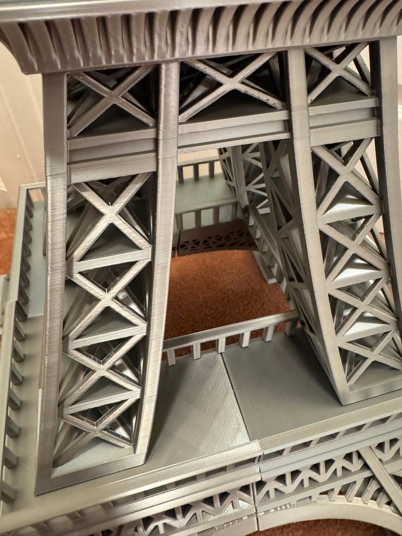 May include: A detailed, gray model of the Eiffel Tower, showcasing its intricate lattice structure. The image highlights the tower's architectural design, with visible cross-bracing and support beams. The model is a miniature representation of the iconic landmark.
