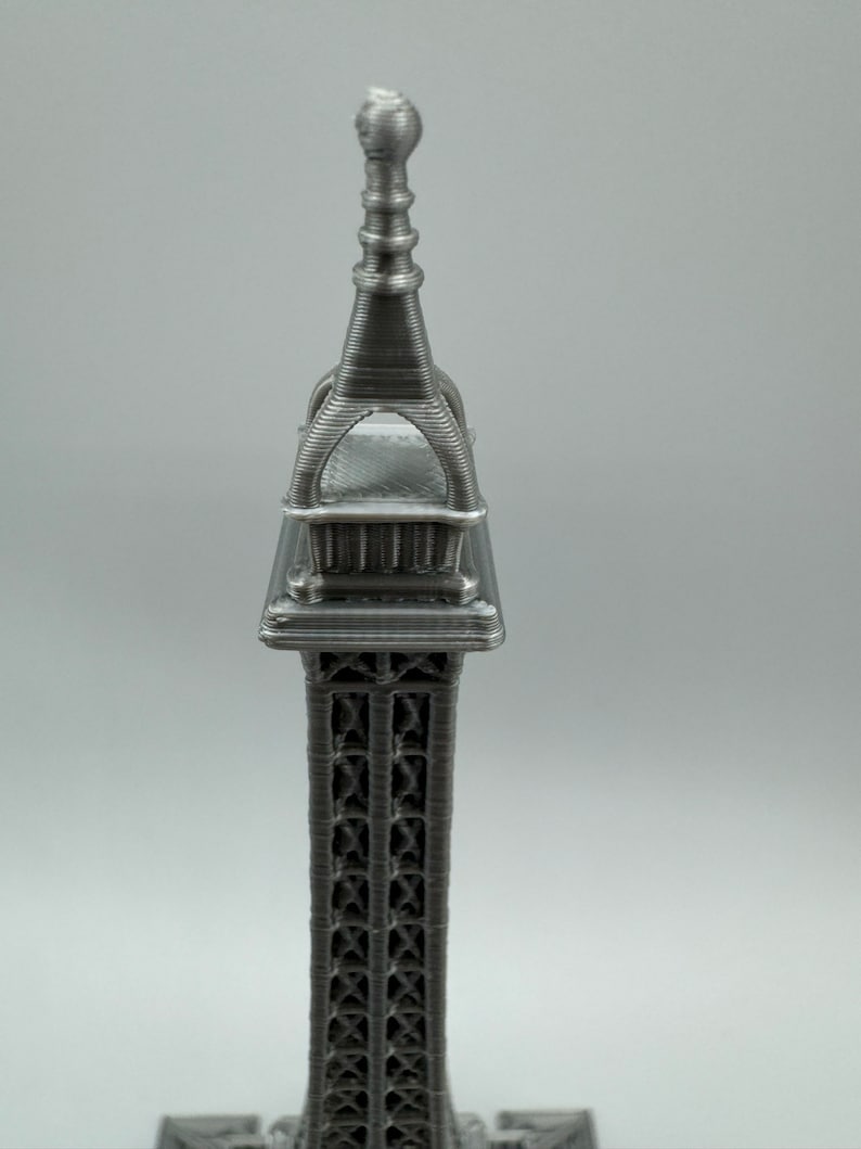 May include: A silver metal Eiffel Tower replica with intricate details. The tower is a popular souvenir and decorative item.