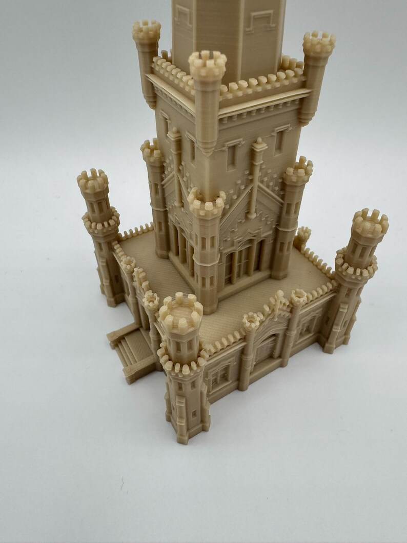 May include: A beige 3D-printed model of a castle with multiple turrets and architectural details. The model features a central tower and several smaller towers, showcasing intricate design elements and a detailed facade. The overall structure is a miniature representation of a historical building.