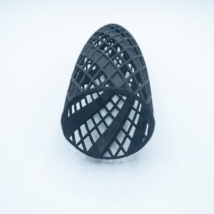 May include: A black, 3D printed, geometric, cylindrical shaped object with a lattice design.