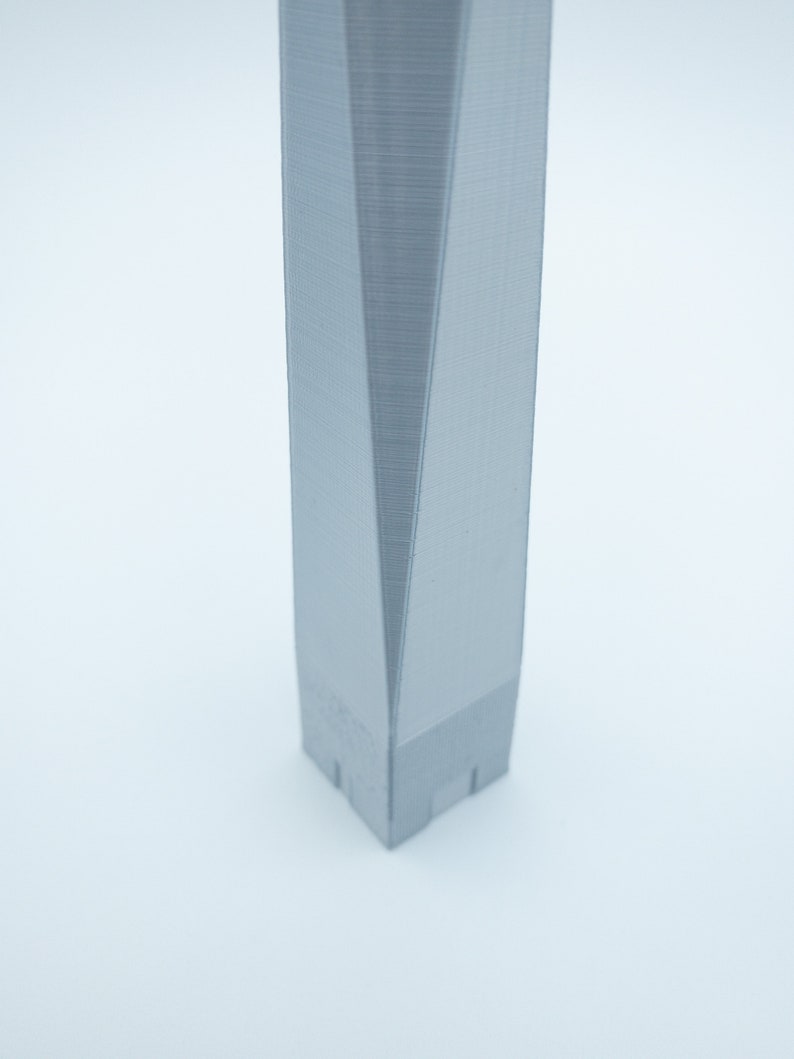 May include: A close-up of a gray, 3D printed model of a skyscraper. The model is detailed and has a sharp, angular design.