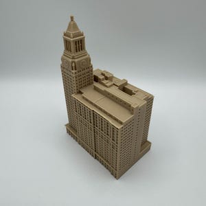 May include: A tan-colored architectural model of a tall building with a clock tower. The model has many windows and detailed architectural features. The building is a replica of a famous landmark.