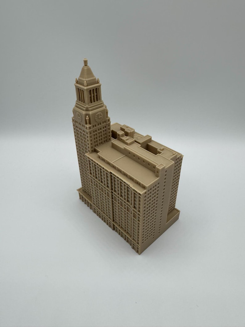May include: A tan-colored architectural model of a tall building with a clock tower. The model has many windows and detailed architectural features. The building is a replica of a famous landmark.