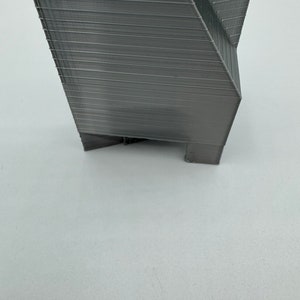 May include: A gray 3D printed object with a geometric design. The object has a sharp point at the top and a flat base.