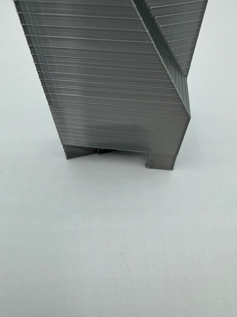 May include: A gray 3D printed object with a geometric design. The object has a sharp point at the top and a flat base.
