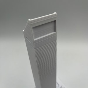 May include: A white 3D printed model of a skyscraper with a flat roof and a rectangular window.