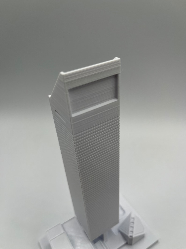 May include: A white 3D printed model of a skyscraper with a flat roof and a rectangular window.