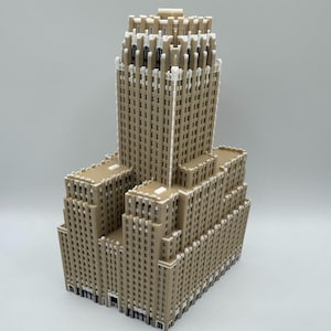 May include: A tan and white architectural model of a skyscraper. The building has a tiered design with a central tower and multiple lower sections. The model is detailed with window and facade features.
