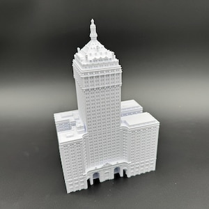 Puede incluir: Maqueta arquitect&oacute;nica blanca de un edificio alto. El modelo presenta una base rectangular, una torre central y una parte superior decorativa. El edificio tiene muchas ventanas y detalles arquitect&oacute;nicos.