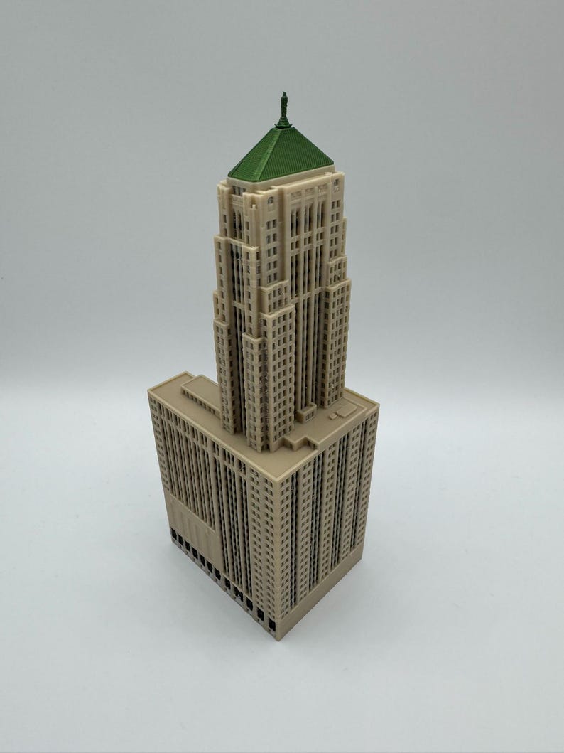 May include: A beige architectural model of a skyscraper with a green roof and a small statue on top. The building has many windows and is a detailed replica of a famous structure.