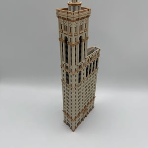 May include: A detailed model of a tall building with a beige facade and brown trim. The building has many windows and a decorative top. The model is standing upright on a white surface.
