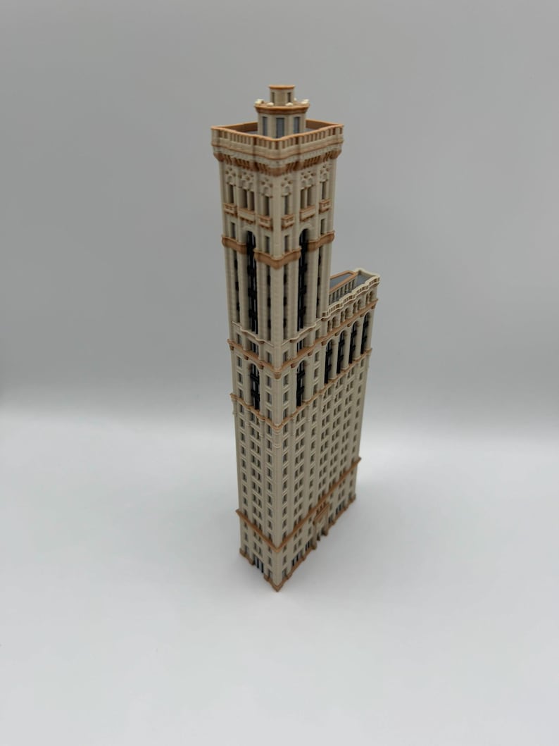 May include: A detailed model of a tall building with a beige facade and brown trim. The building has many windows and a decorative top. The model is standing upright on a white surface.