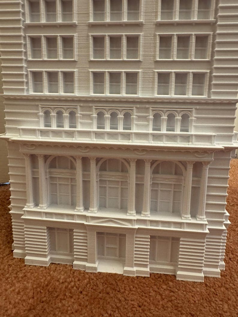 Op de afbeelding: Een wit 3D-geprint model van een gebouw met meerdere ramen en decoratieve details. Het gebouw heeft een plat dak en een eenvoudige gevel.