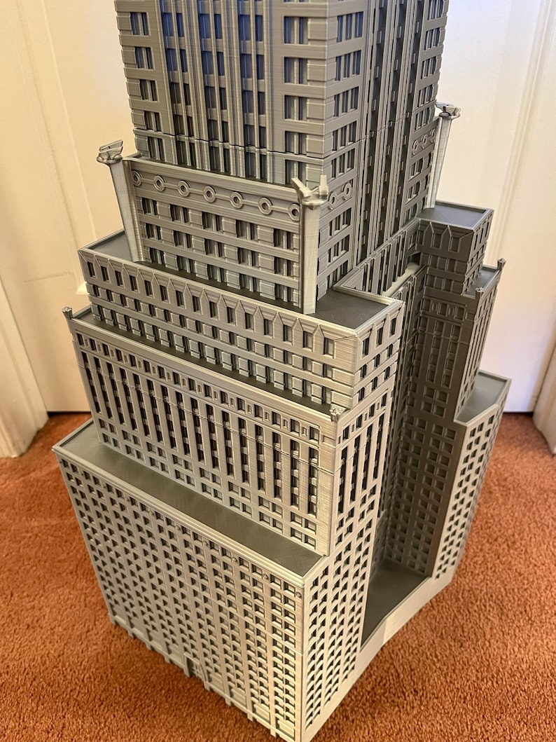 May include: A detailed model of a tall, gray skyscraper with many windows and decorative details. The model is made of plastic and is about 12 inches tall.