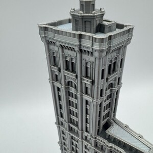 May include: A grey 3D-printed model of a tall building with detailed architecture. The building has multiple storeys, arched windows, and decorative features. The model is a miniature replica of a famous skyscraper.