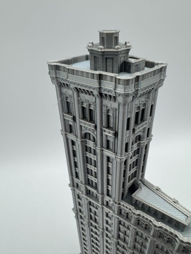 May include: A grey 3D-printed model of a tall building with detailed architecture. The building has multiple storeys, arched windows, and decorative features. The model is a miniature replica of a famous skyscraper.