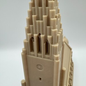 May include: A beige 3D-printed model of a church with a tall, tiered tower. The tower has arched windows and a detailed facade. The model is made of a light-colored material and is set against a plain background.