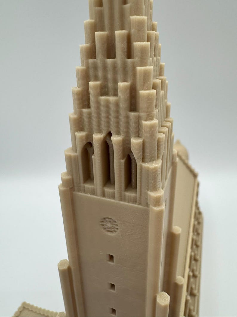 May include: A beige 3D-printed model of a church with a tall, tiered tower. The tower has arched windows and a detailed facade. The model is made of a light-colored material and is set against a plain background.