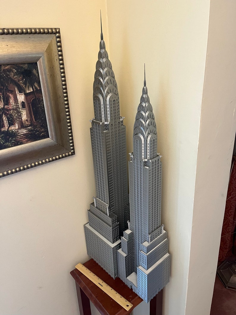 May include: A silver model of the Chrysler Building in New York City. The model is made of plastic and is about 12 inches tall. It is a detailed replica of the building, including the spire and the Art Deco details.