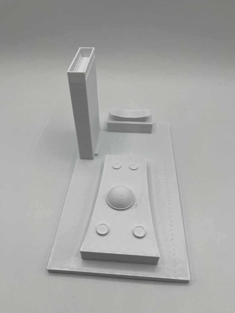 K&ouml;nnte beinhalten: Wei&szlig;es 3D-gedrucktes Modell einer Stadtlandschaft mit einem hohen Geb&auml;ude, einem kuppelf&ouml;rmigen Bauwerk und einem gebogenen Geb&auml;ude. Das Modell steht auf einem wei&szlig;en Sockel.