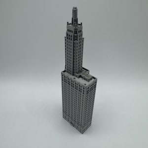 May include: A grey 3D printed model of a tall skyscraper building with a pointed roof and many windows.