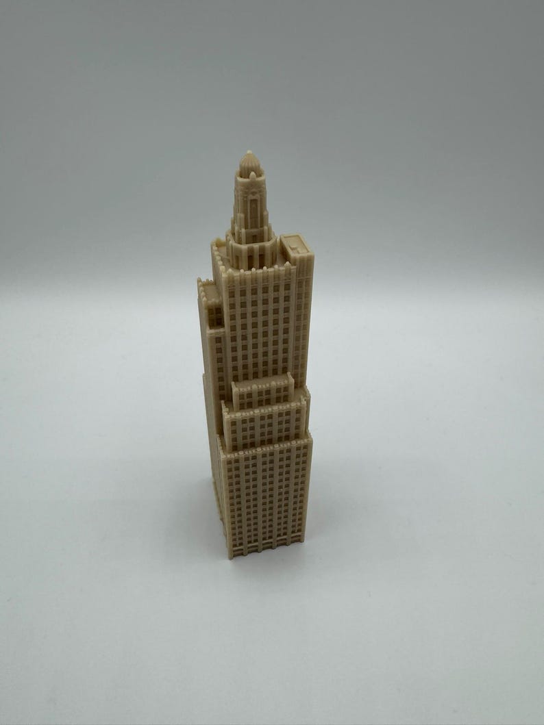 May include: A tan-colored miniature skyscraper model with intricate architectural details. The model features multiple levels, windows, and a detailed top section with a dome. The building is a representation of a classic architectural style.