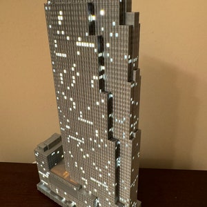 May include: A detailed model of a skyscraper with a gray facade and illuminated windows. The model is made of plastic and has a realistic design.
