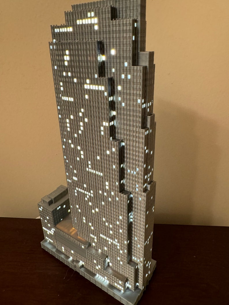 May include: A detailed model of a skyscraper with a gray facade and illuminated windows. The model is made of plastic and has a realistic design.