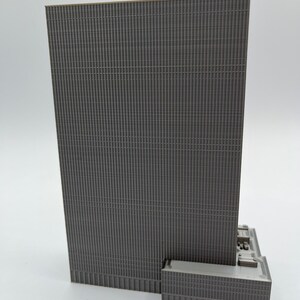 May include: A gray 3D printed model of a skyscraper with a textured facade. The model is detailed with a small base and a rooftop.